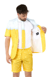 A man models the Suitmeister Premium Beer Yellow novelty suit, featuring bubble-patterned yellow shorts and jacket with a white shirt and tie. He holds open the jacket to reveal its fun inner lining.