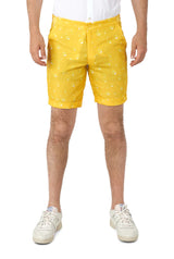 A person is wearing Suitmeisters Premium Beer Yellow shorts, featuring a water droplet pattern, paired with a tucked-in white shirt and white sneakers, posed against a white background.