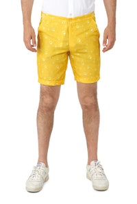 A person is wearing Suitmeisters Premium Beer Yellow shorts, featuring a water droplet pattern, paired with a tucked-in white shirt and white sneakers, posed against a white background.