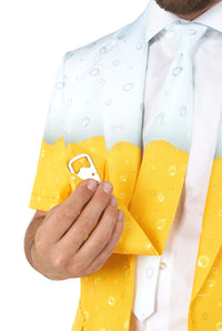 A man wears Suitmeisters Premium Beer Yellow suit, featuring a beer foam and bubbles design, paired with a matching tie and white shirt. A silver bottle opener peeks from his chest pocket. The yellow suit has white tips, resembling a glass of beer.