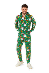 A man smiles while wearing the Suitmeister "Santa Elves Green - Christmas onesie," featuring Santa Claus, stars, and presents. He stands with his hands behind his back in white sneakers against a plain white background.