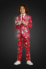 A child confidently wears the Suitmeister BOYS Christmas Red Icons - Light Up suit, featuring festive snowmen and tree patterns, paired with a white shirt, red tie, and white sneakers against a dark background.