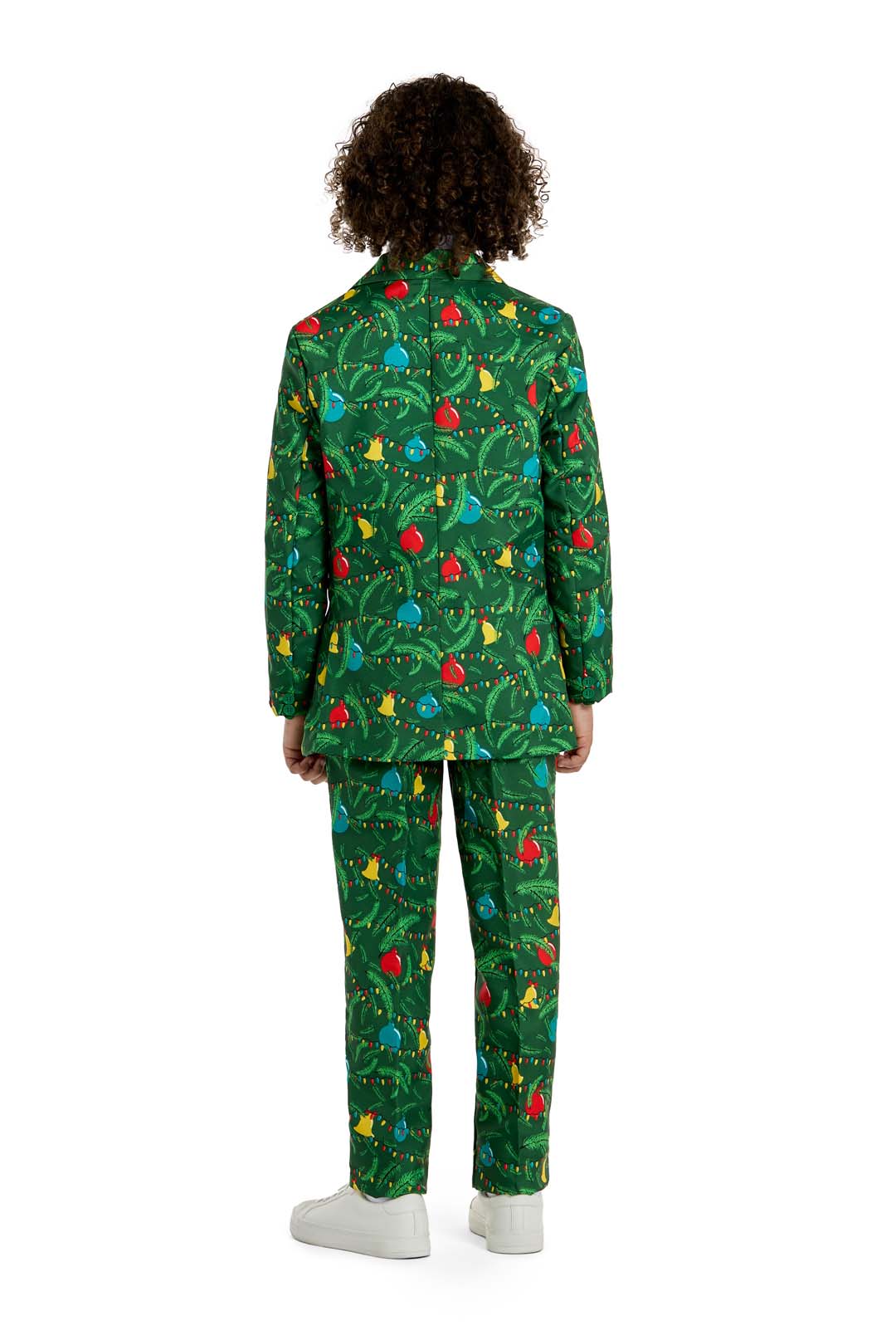 A boy with curly hair faces away, wearing the Suitmeister BOYS Christmas Green Tree - Light Up suit decorated with ornaments and tree patterns, plus white shoes. The background is plain white.