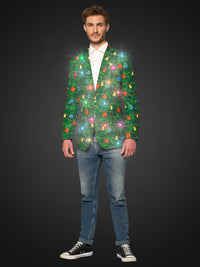 A man stands against a dark background wearing blue jeans, black sneakers, and the Suitmeister Christmas Green Tree - Light Up blazer, decorated with glowing Christmas lights and ornaments.