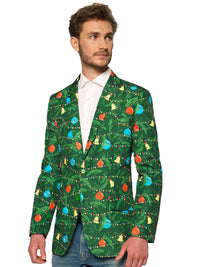 A man wears the Suitmeister Christmas Green Tree - Light Up blazer, adorned with colorful ornaments and garlands, over a white shirt and jeans while looking to his right.