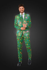 A man smiles while wearing the Suitmeister Christmas Green Tree - Light Up suit, featuring colorful decorations, twinkling lights, a matching tie, and black shoes against a dark background.