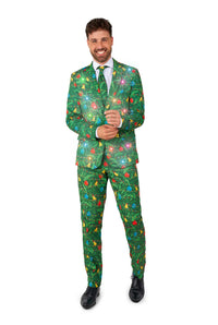 A smiling man wears the Suitmeister Christmas Green Tree - Light Up suit, featuring a green jacket with Christmas tree patterns and twinkling lights, paired with a white shirt, matching tie, and black dress shoes.