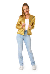 A smiling woman poses against a white background, wearing the Suitmeister Sequins Gold sequin blazer over a white top with light blue jeans and white sneakers, holding the blazer’s lapels in both hands.