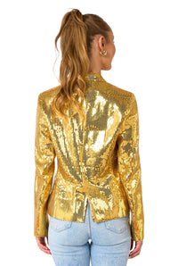 A woman with long, wavy hair in a ponytail models the Suitmeister Sequins Gold - Sequins blazer with light blue jeans, standing with her back to the camera against a white background.
