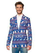 A smiling man is wearing the Christmas Blue Nordic Jacket, a festive blazer from Suitmeister, adorned with a holiday pattern featuring reindeer, snowflakes, and trees. He pairs it with a white shirt and jeans.