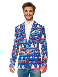 A smiling man is wearing the Christmas Blue Nordic Jacket, a festive blazer from Suitmeister, adorned with a holiday pattern featuring reindeer, snowflakes, and trees. He pairs it with a white shirt and jeans.