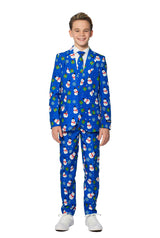 A young boy is beaming with joy in a Suitmeister's Christmas Suit Blue Snowman. The festive attire features a cheerful Christmas-themed pattern adorned with snowmen, holly, and presents. He stands against a plain white background while wearing white shoes.