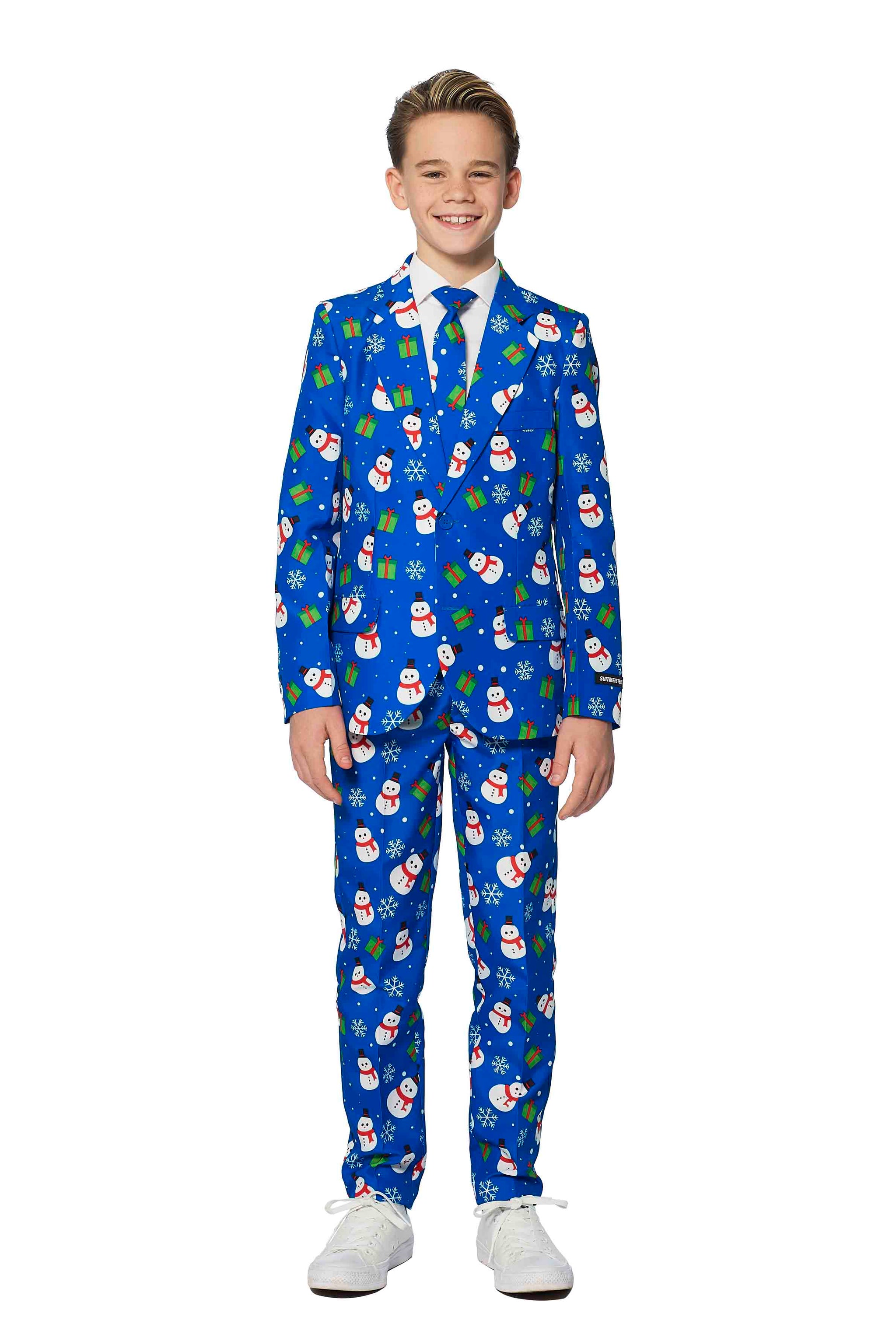 A young boy is beaming with joy in a Suitmeister's Christmas Suit Blue Snowman. The festive attire features a cheerful Christmas-themed pattern adorned with snowmen, holly, and presents. He stands against a plain white background while wearing white shoes.