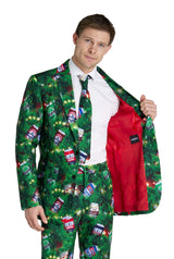 A man models the Suitmeister Christmas Beers Green suit, featuring a green pine branch and beer can pattern, with a bright red lining visible as he opens his jacket. He stands against a plain white background.